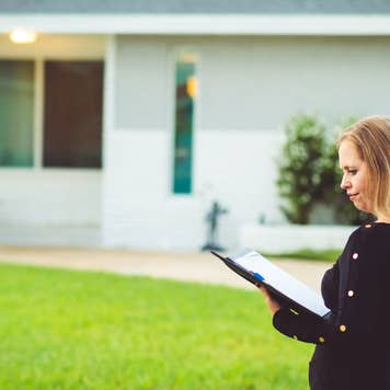 Woman walking by a house while looking at documents