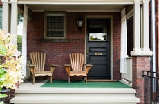 Two wooden outdoor chairs on the porch of an old style home.