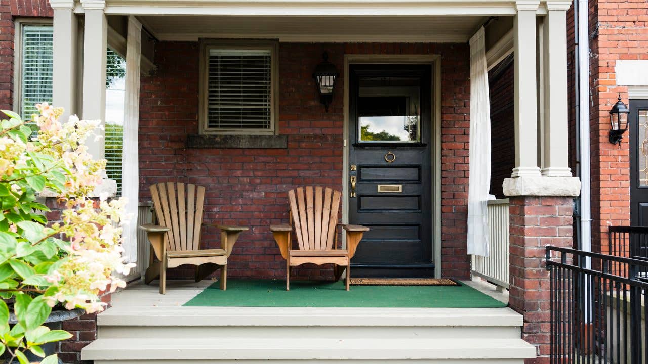 Two wooden outdoor chairs on the porch of an old style home.
