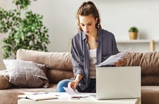 Calm focused female freelancer in casual clothes revising reports while sitting on soft couch at table and using computer in light contemporary apartment