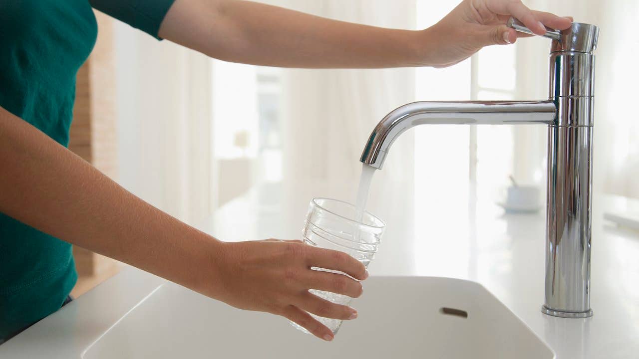 Person pouring a glass of water from a faucet