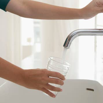 Person pouring a glass of water from a faucet