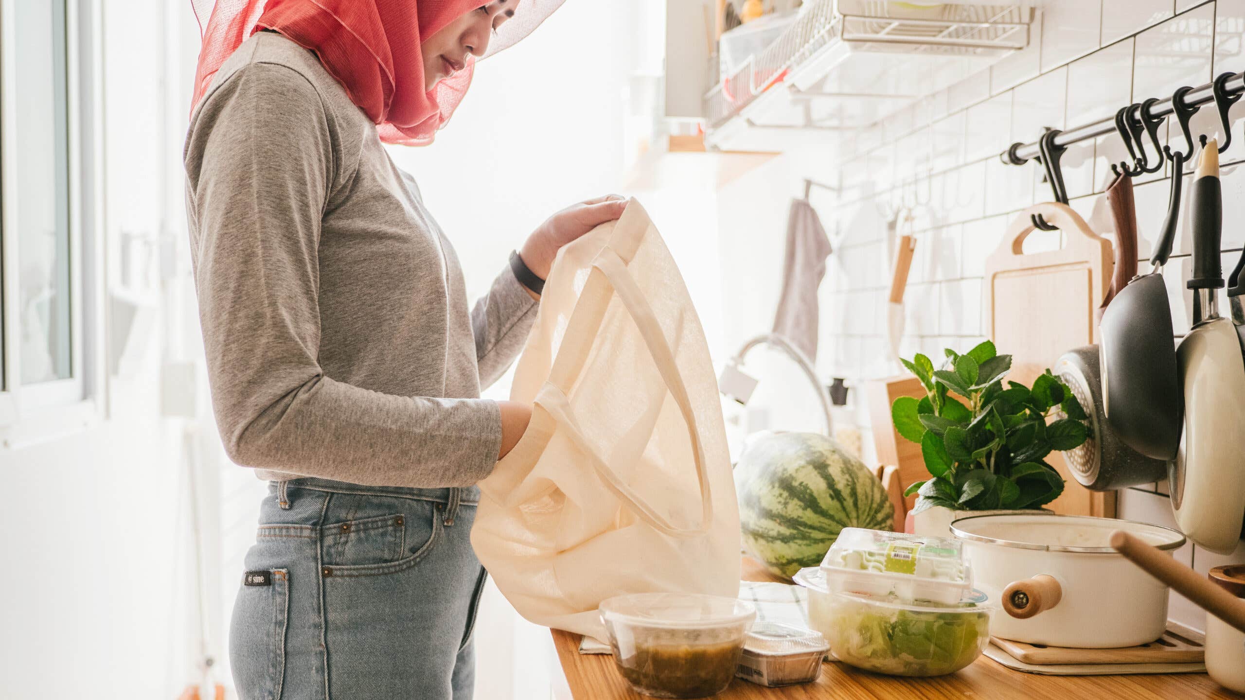 Islam woman unloading fresh vegetables from her reusable shopping bag at home.