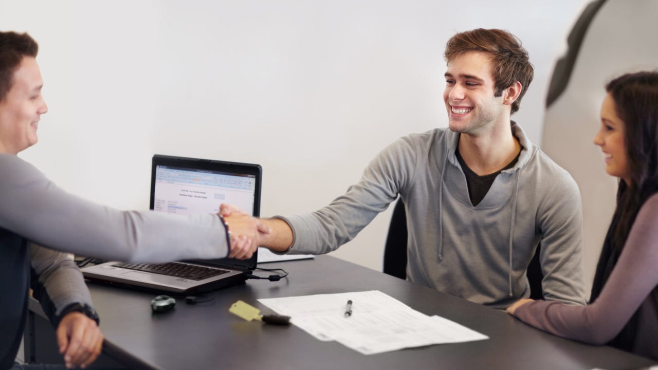 Couple sitting at desk across from car salesperson, smiling and shaking hands