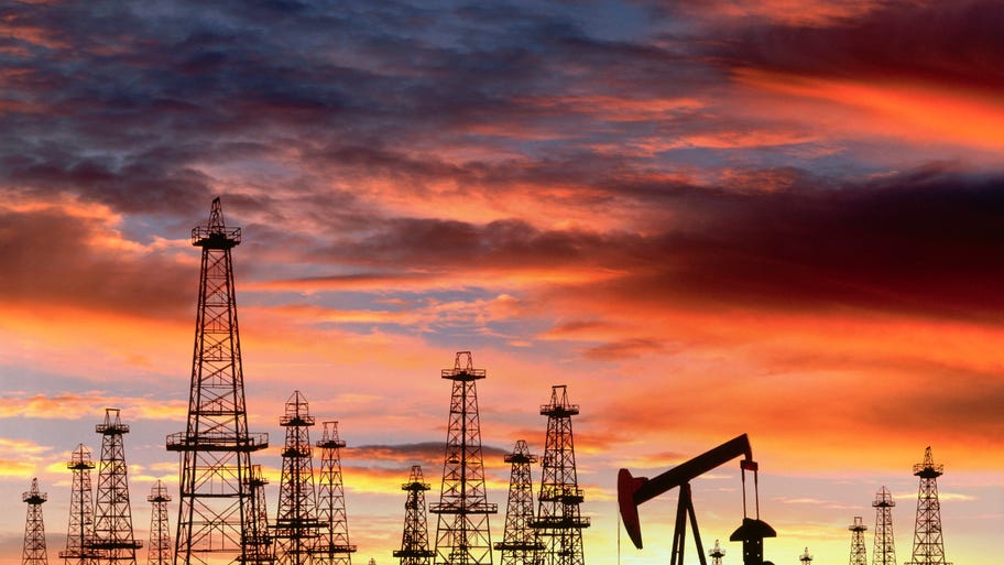 Oil derricks are silhouetted by a sunset