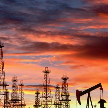 Oil derricks are silhouetted by a sunset