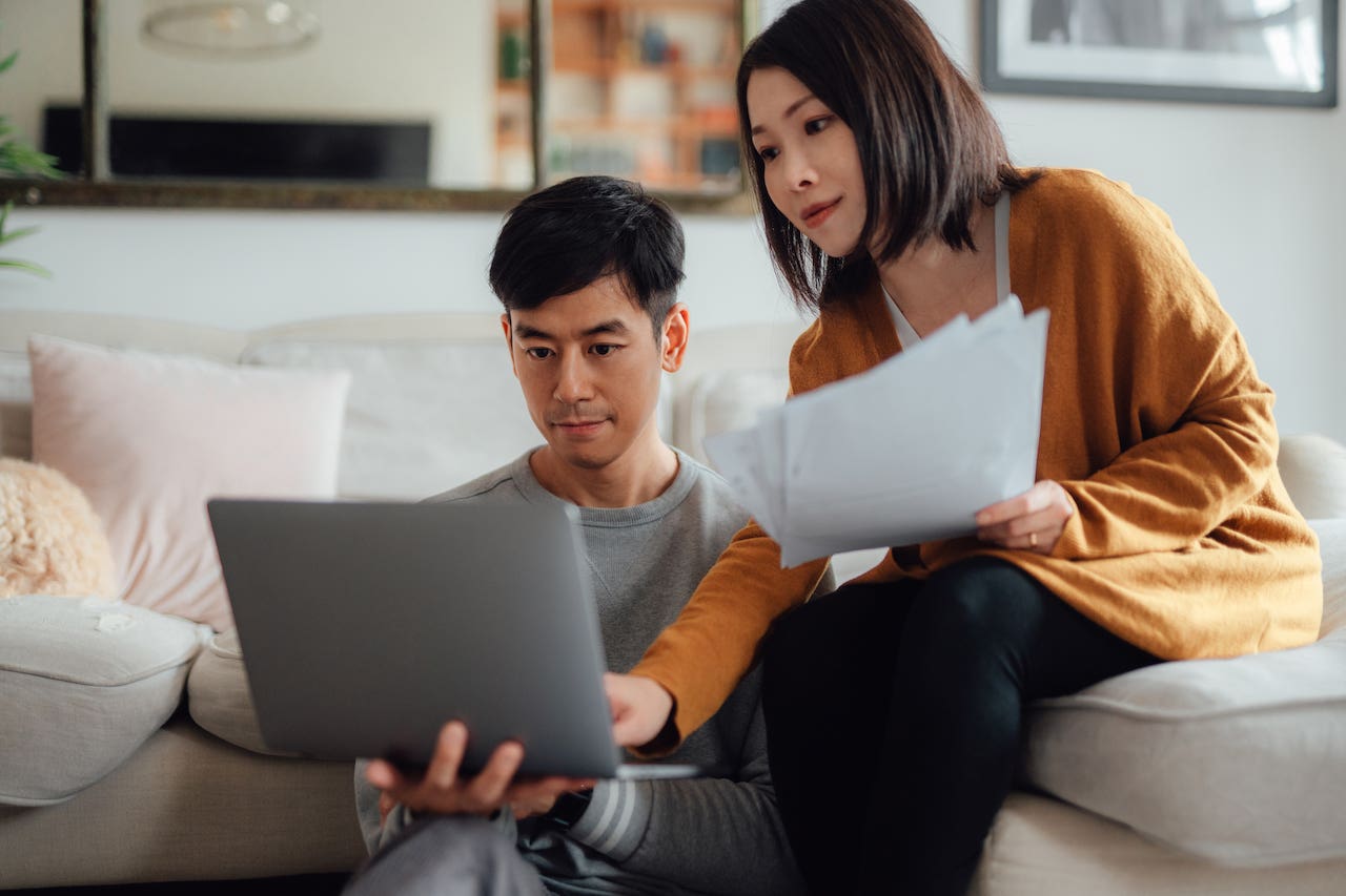 Serious looking young couple discussing over financial bills while using laptop in living room.