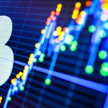 Computer illustration of Bitcoin logo juxtaposed against neon colored financial charts
