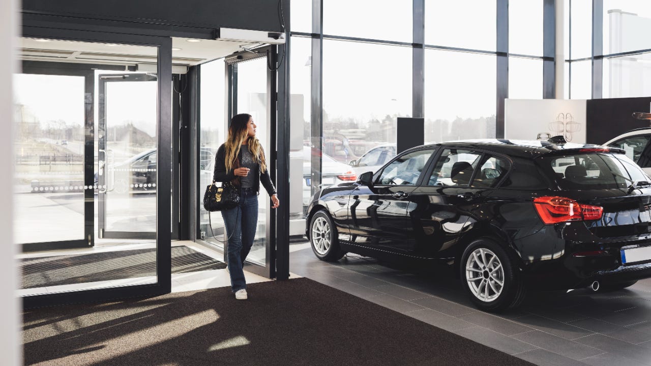 Woman walking into car dealership with black car to the right