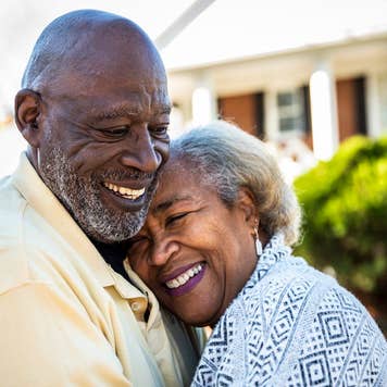 Older african-american couple smiling and embracing in front of a brick home with white pillars