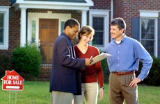 Three people looking over documents in front of a house for sale