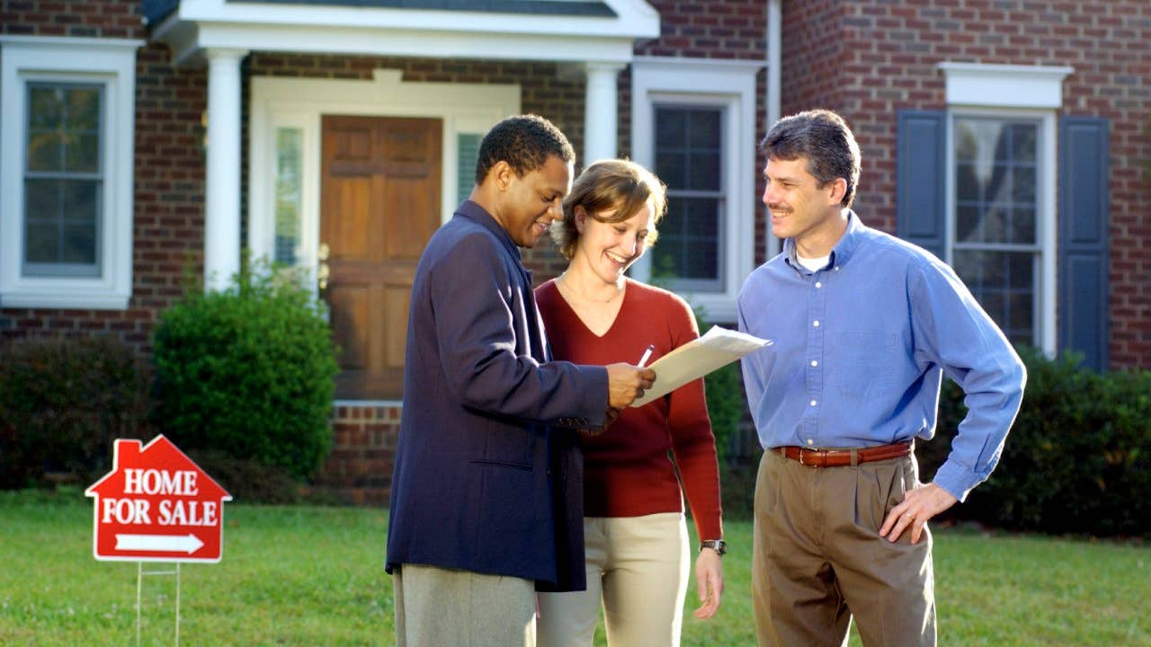 Three people looking over documents in front of a house for sale