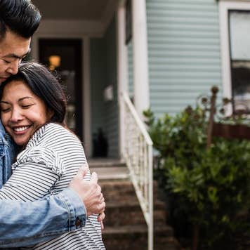 Couple hugging outside of light blue family home with a white railing leading up the front steps