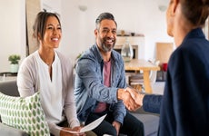 Smiling couple holds paperwork and shakes hands with a real estate agent