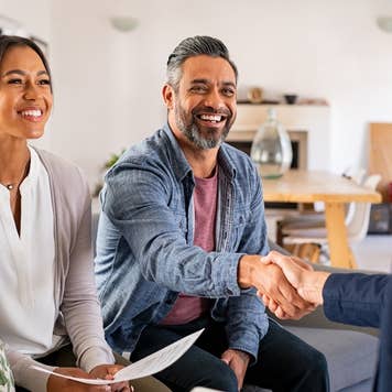 Smiling couple holds paperwork and shakes hands with a real estate agent
