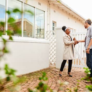 Two people shaking hands in front of a house