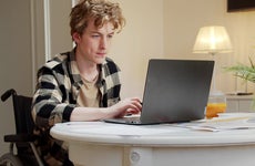 Young Man Sitting On Wheelchair Using Laptop