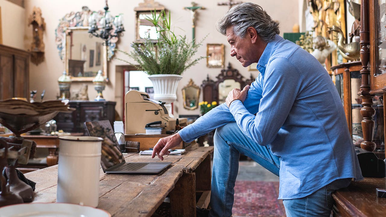 Mature male owner of antique store using laptop in his shop