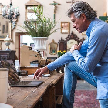 Mature male owner of antique store using laptop in his shop