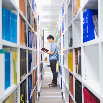 Student stands between stacks in a library