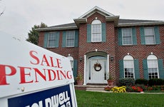 A Coldwell Banker "sale pending" sign outside of a colonial style red brick home with green shutters