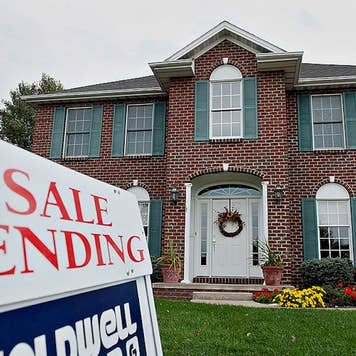 A Coldwell Banker "sale pending" sign outside of a colonial style red brick home with green shutters