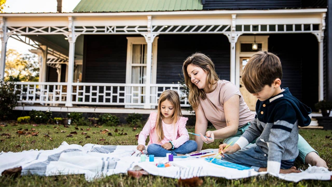 Mother helping children paint in front yard of rural farmhouse