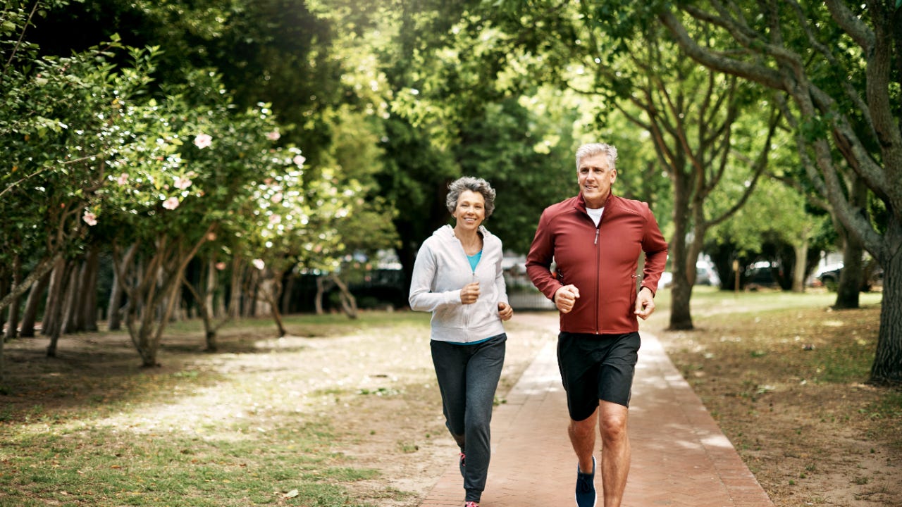 An older couple is jogging in a park