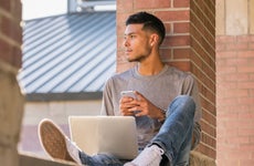 College student sits outside with laptop and cellphone