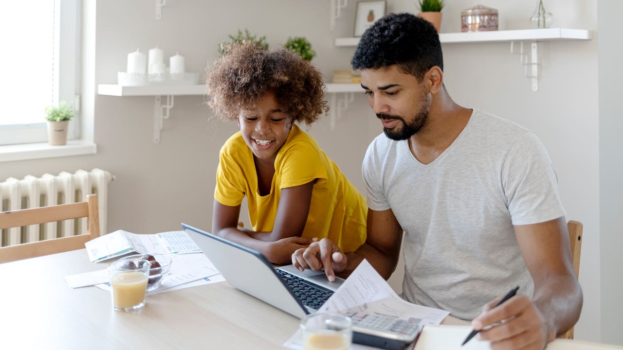 father working on computer and paperwork next to daughter