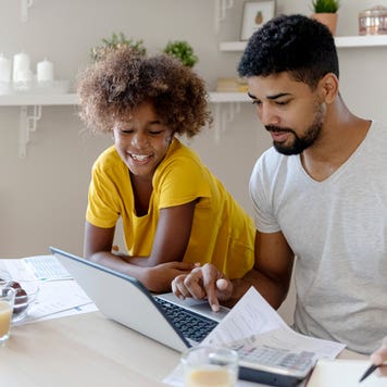 father working on computer and paperwork next to daughter