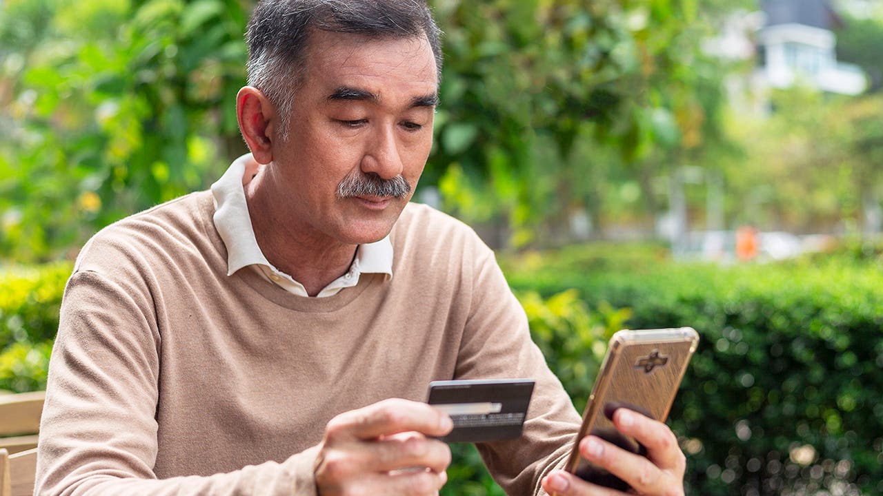 Elderly man is paying online by using smart phone and credit card