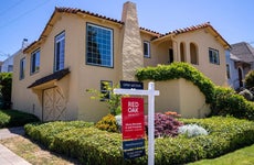 A red for sale sign from red oak realty outside a mediterranean style home with lush landscaping and a tile roof