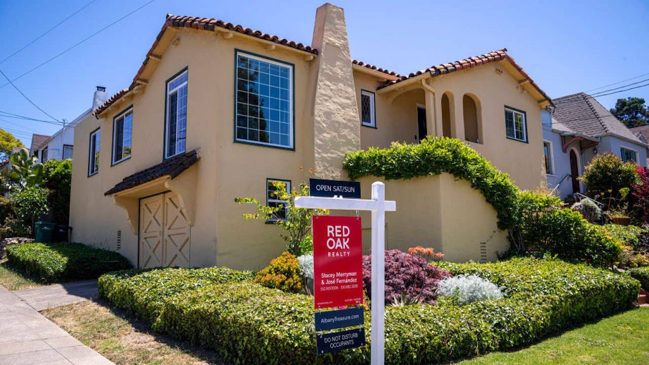 A red for sale sign from red oak realty outside a mediterranean style home with lush landscaping and a tile roof