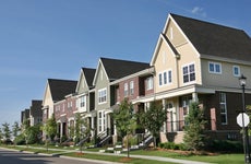 A row of tidy suburban townhouses, with newly planted trees and a blue sky