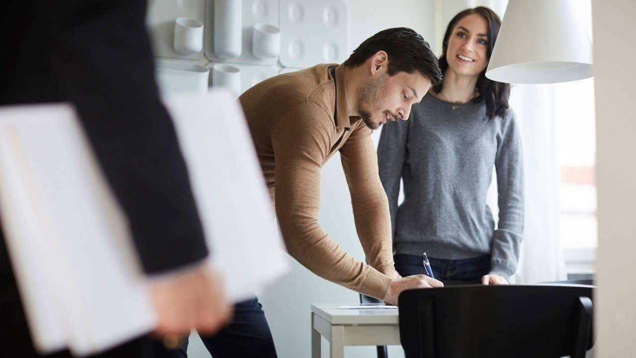 Woman looking at real estate agent while man signing documents at new home