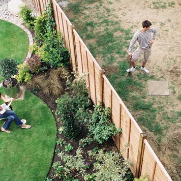 Woman sitting on one side of a yard while a man with a shovel stands, divided by a fence