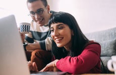 Woman smiling at laptop with man smiling and looking over her shoulder