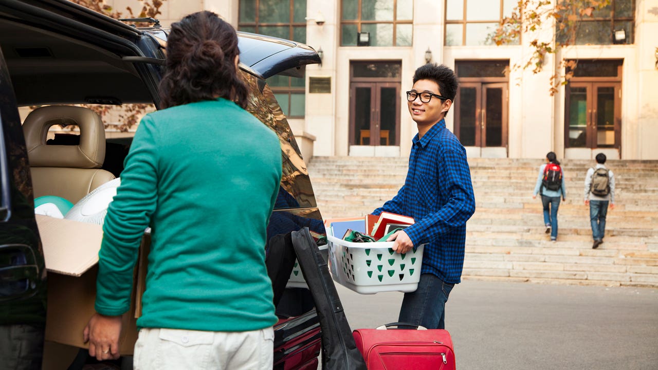 A child heading off to college holding their supplies while their parent bids them farewell.