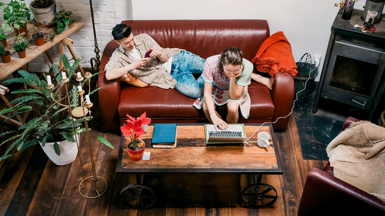 couple sitting together on the couch and working on laptop and phone