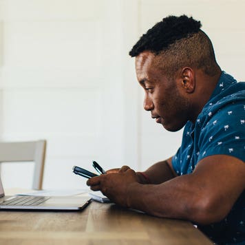 man sitting at a table and looking at his laptop and phone