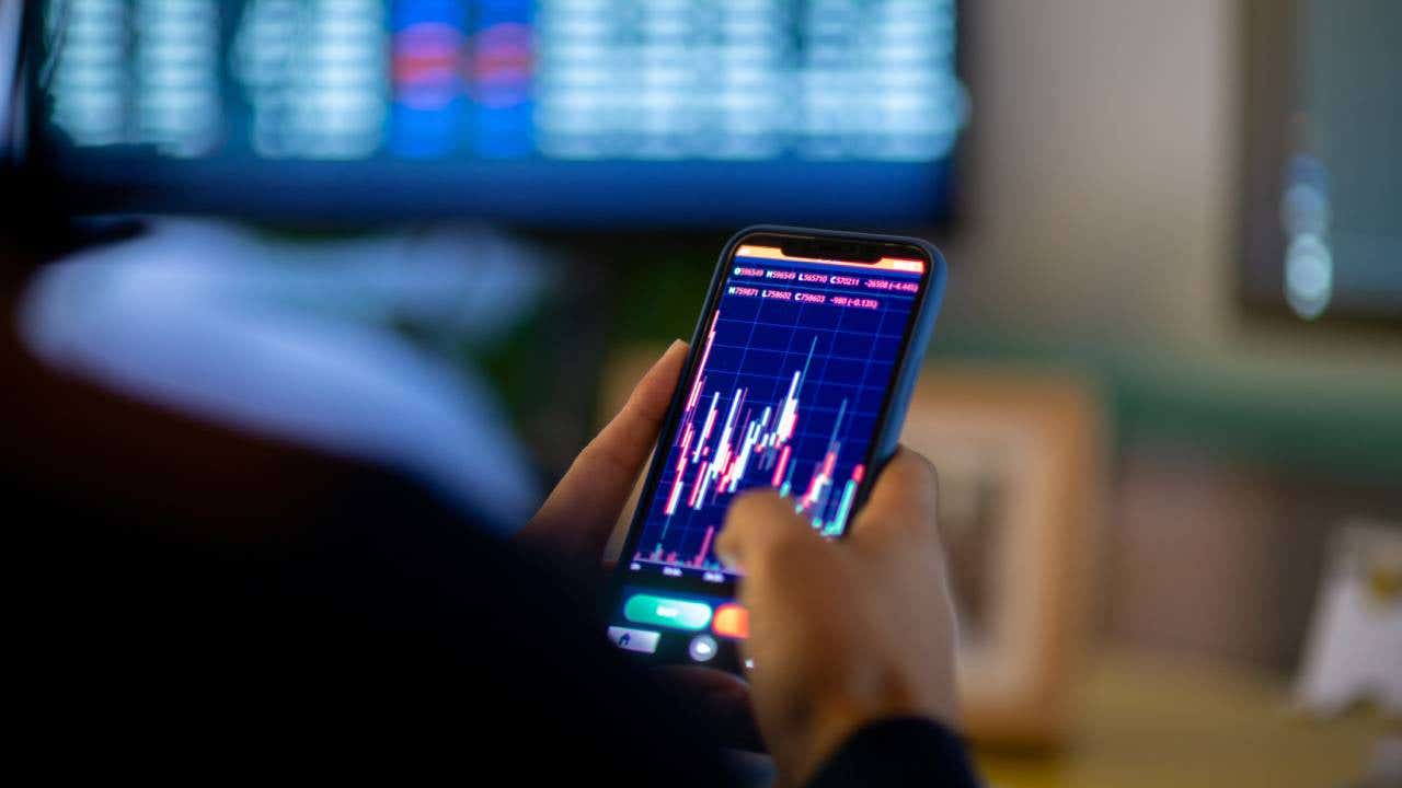 Man looking at currency trading app on his smart phone from his home office