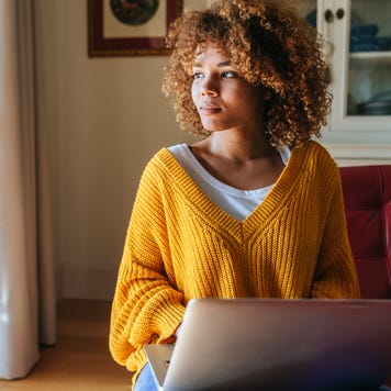 Young woman sitting on chaiselongue using laptop at home