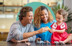 Mixed-race family playing with toy dinosaurs with their child.