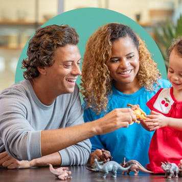 Mixed-race family playing with toy dinosaurs with their child.