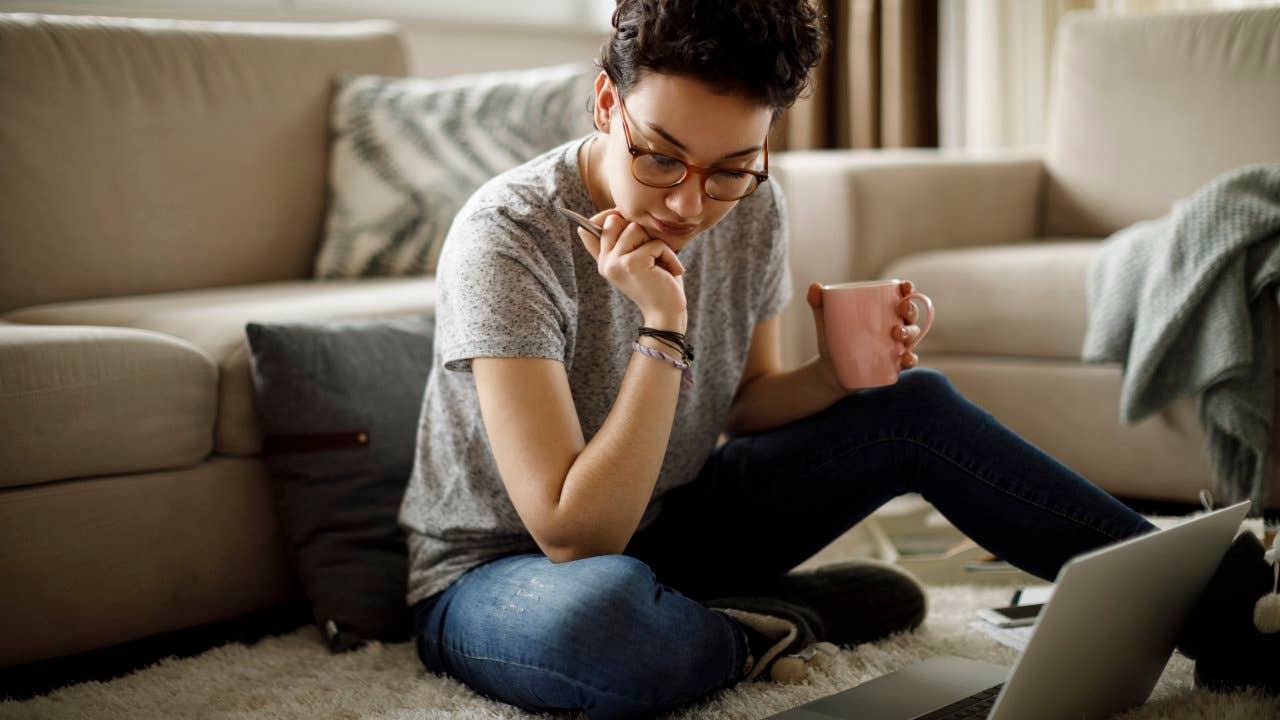 Woman reviewing documents on a laptop while sitting on the floor