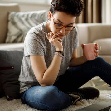 Woman reviewing documents on a laptop while sitting on the floor
