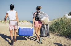 Two people carrying a blue cooler on the beach