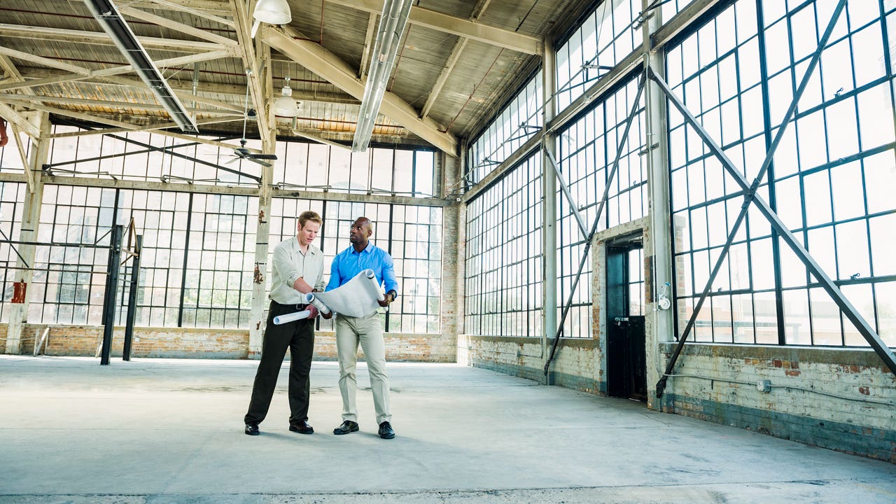 Businessmen reading blueprints in empty warehouse
