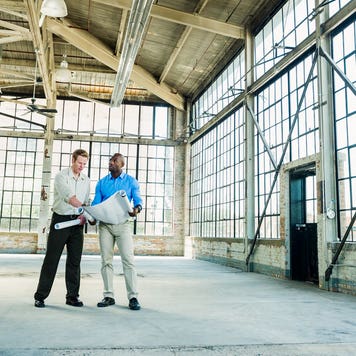 Businessmen reading blueprints in empty warehouse